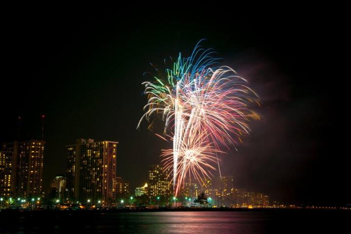 fireworks at night over the ocean with city in background