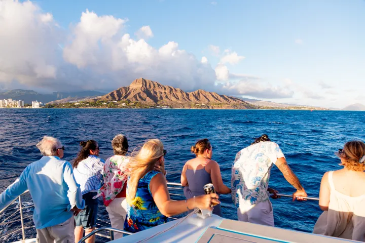 People on a boat admire a mountain view over the ocean.