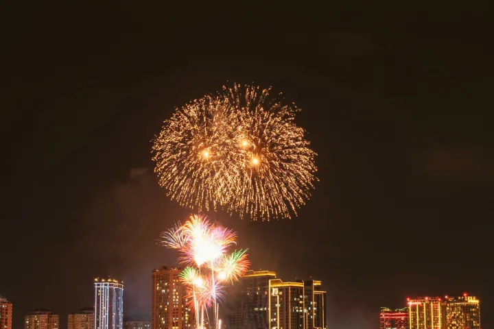 Colorful fireworks over a city skyline at night, reflecting on water.