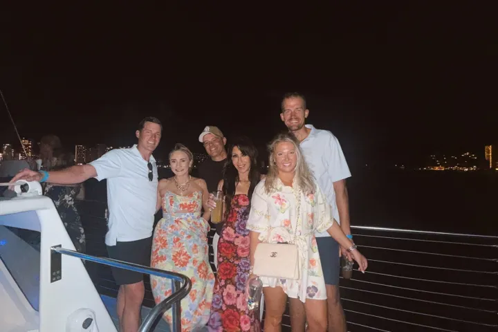 Group of six people posing on a boat deck at night, with city lights in the background.
