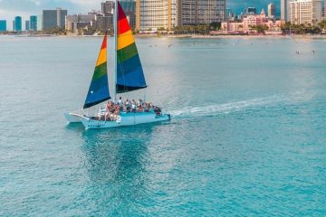 boat with rainbow sail on water with city in background at daytime