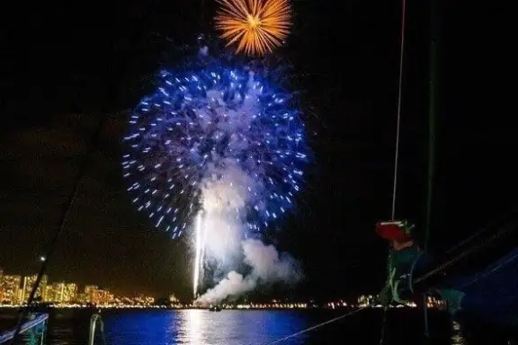 Fireworks display over a city skyline at night, viewed from a boat on the water.